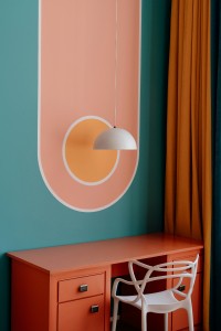 Bureau en bois orange avec pan et une chaise design avec un pan de mur bleu avec des formes géométrique rose et jaune clair