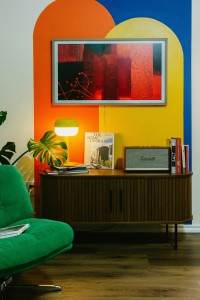 Salon avec des formes géographiques peintes sur le mur jaune orange et bleu et du mobilier en bois et en tissu pour donner un style rétro